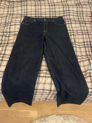 Mörkblå wide leg jeans Canard - Säljer ett par mörkblå wide leg jeans från Canard Collection i storlek 42. Jeansen har klassisk femficksdesign, raka och vida ben samt kontrastsömmar. Perfekta för dig som gillar en avslappnad och trendig look. Materialet är klassisk denim.