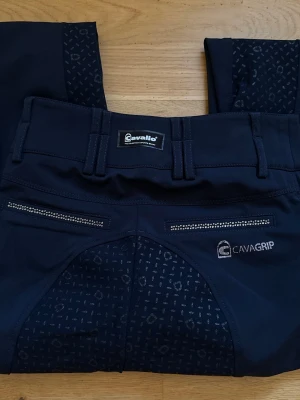 Mörkblå ridbyxor från Cavallo - Snygga mörkblå helskodda ridbyxor från Cavallo med fina detaljerl. Byxorna har breda hällor, Cavallo-logga i strass och extra grepp på sätet för bättre komfort vid ridning. Perfekta för dig som vill ha stil och funktion i stallet.