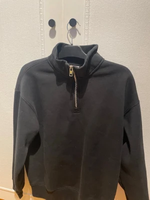 Svart half-zip hoodie från H&M - En svart hoodie från H&M i relaxed fit med halv dragkedja framtill. Tillverkad i mjukt sweatshirtmaterial och har hög krage. Perfekt för en chill och avslappnad stil. Passar till det mesta och är enkel att matcha med andra plagg.