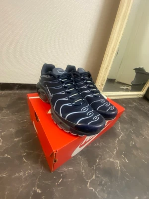 Nike TN sneakers - Nike TN  sneakers  i marinblått med vita vågformade linjer över hela ovandelen. Skorna har snörning och en sportig, chunky sula. Perfekta för dig som gillar en modern och unik look. Materialet är syntet och textil.