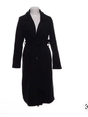 Marinblå lång kappa  - Stilren marinblå lång kappa med klassisk krage och knytskärp i midjan. Kappan har knäppning framtill och raka ärmar. Perfekt för dig som vill ha en tidlös och enkel look. Materialet ser ut att vara ullblandning. (Gjord av ai) ny med prislapp men köpt på sellpy. 