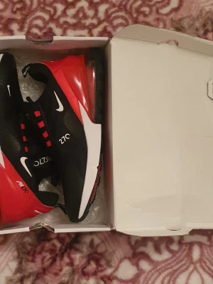 Nike Air Max 270 svart/röd sneakers - Nike Air Max 270 sneakers i svart och rött med vita detaljer. Skorna har en tydlig Air Max-sula baktill, mesh-ovandel och röda snörhål. Snygg design med 270- och Nike-loggor på sidorna. Perfekta för dig som gillar sportig och modern stil. Det står storlek 45 MEN DEN ÄR 1 STORLEK MINDRE SÅ STORLEK 44.