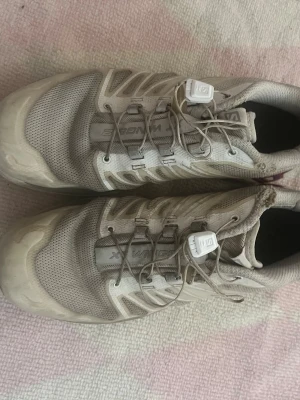 Beige Salomon XT-Wings sneakers - Säljer ett par beige Salomon XT-Wings sneakers med grå och lila detaljer. Skorna har meshpaneler för bra ventilation och snabbsnörning med vit låsning. Perfekta för en sportig och trendig look.