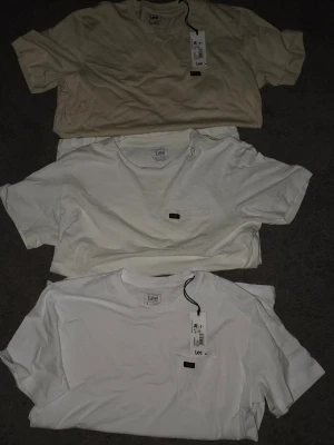 Lee t-shirts. En för 80kr, tre för 220kr - Säljer tre stilrena t-shirts från Lee, två i vitt och en i beige. Två av dem har kvar taggen, dessa är aldrig använda. Alla har klassisk passform, rund hals och korta ärmar. Perfekt för någon som gillar att styla kläder. Vid köp av en t shirt får du ge ett prisförslag på 80kr och välja ut en. Hör av dig vid frågor!