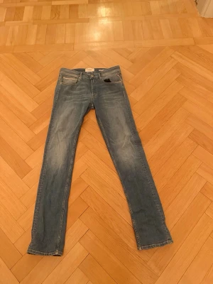 Blå slim fit jeans från Replay - Snygga blå slim fit jeans från Replay med klassisk femficksdesign och diskreta slitningar på benen. Jeansen har normal midja och är tillverkade i mjuk denim med stretch för extra komfort. Perfekta för en avslappnad och trendig look.