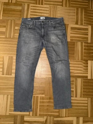 Grå Jack & Jones Regular-fit Jeans - Säljer ett par grå jeans från Jack & Jones med rak passform och klassisk femficksdesign. Jeansen har en snygg tvättad look och är tillverkade i bomull. Perfekta för en avslappnad och trendig stil.