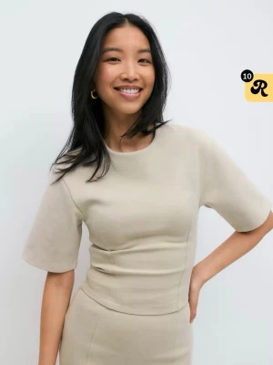 Beige croppad topp från Gina  - Trendig beige croppad topp från Gina med rund halsringning och korta ärmar. Tjockare material som ger en snygg form och markerad midja. Perfekt att styla med både jeans och kjol för en clean look.