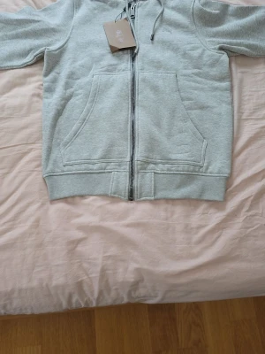 Ljusgrå zip hoodie från Burberry  - Ljusgrå hoodie med dragkedja från Burberry Klassisk modell med huva och justerbara snören, stora kängurufickor framtill och ribbade muddar. Tillverkad i mjuk bomullsblandning för skön känsla. Perfekt för en chill och stilren look.