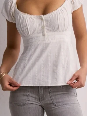 Vit blus med puffärm och knappar - Supersöt vit blus med korta puffärmar och knappar framtill. Blusen har en markerad midja och lätt rynkade detaljer upptill. Perfekt att styla med jeans eller kjol för en fräsch look.