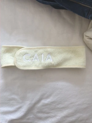 Gulvit hårband från CAIA - Säljer ett mjukt och stretchigt hårband från CAIA i gulvit färg. Perfekt för att hålla håret borta vid sminkning eller hudvård. Kardborrestängning gör det enkelt att justera storleken. Broderad logga framtill.