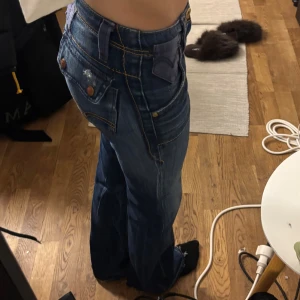 Blå bootcut jeans från Levi's - Säljer ett par blå bootcut jeans från Levi's med markerade sömmar och stora fickor med knappar bak. Jeansen har låg midja.
