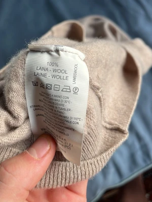 Beige stickad tröja i 100% ull - Säljer en beige stickad tröja i 100% lammull. Tröjan har en mjuk och klassisk look med ribbade muddar vid ärmslut och nederkant. Perfekt för dig som gillar naturliga material och enkel stil.