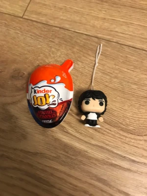 Kinder Joy och figurnyckelring - Säljer ett Kinder Joy Mike som är en liten svartvit figurnyckelring med snöre. Perfekt för dig som gillar samlarprylar eller vill ha en rolig accessoar till väskan. Figuren har svart hår och vita detaljer på kläderna.