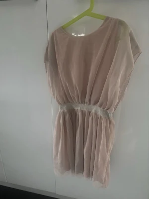 Ljusrosa kortklänning med glittermidja - Söt ljusrosa kortklänning med transparent tyll och glittrigt resårband i midjan. Klänningen har en lös passform och är ärmlös, perfekt för en somrig look. Materialet känns lätt och luftigt.