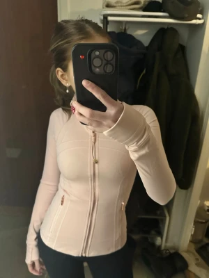Lululemon define jacket  - Snygg ljusrosa träningsjacka ifrån lululemon med hel dragkedja framtill och två fickor med dragkedja. Figurnära passform och långa ärmar. Perfekt för gymmet eller löprundan. Materialet är stretchigt och bekvämt.