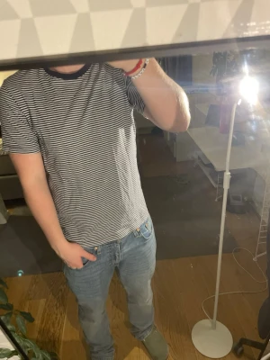 Randig svartvit t-shirt i bomull - Säljer en stilren svartvit randig t-shirt med smala horisontella ränder och svart ribbad krage. T-shirten har korta ärmar och är gjord i mjuk bomull, perfekt för en avslappnad look.