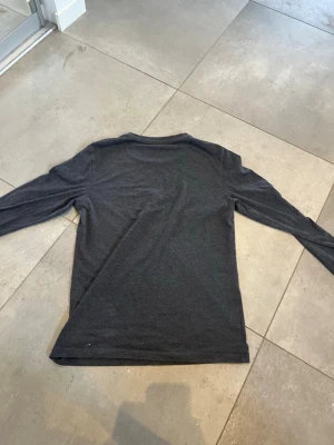 Mörkgrå långärmad tröja - En basic mörkgrå långärmad tröja med rund halsringning. Tröjan är enkel i modellen och passar perfekt till lager-på-lager-stil. Tillverkad i ett mjukt och bekvämt material som känns skönt mot huden.