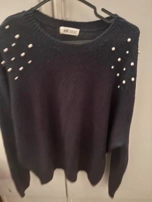 Mörkblå stickad tröja med pärlor - Säljer en mörkblå stickad tröja från H&M med dekorativa vita pärlor på axlarna. Tröjan har rund halsringning och långa ärmar. Perfekt för dig som vill ha något både snyggt och bekvämt till hösten eller vintern. För mer bilder/justering av pris skriv gärna❤️🤗