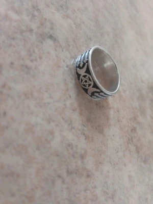 Bred silverfärgad ring med pentagram - Cool bred ring i silverfärgad metall med svart bakgrund och detaljerade mönster, inklusive ett pentagram och månsymboler. Perfekt för dig som gillar alternativ stil och unika smycken. Ringen har en robust känsla och sticker verkligen ut. Ringen är 18.1mm och är i äkta silver. Finns en 925 sterling silver stämpel på insidan av ringen.
