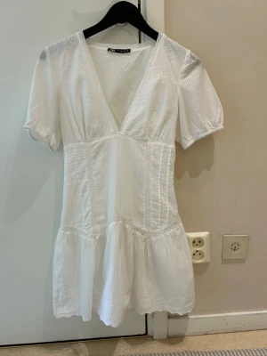  Slutsåld Vit kort klänning från Zara - Söt vit kort klänning från Zara med v-ringning och broderade detaljer på bröstet. Klänningen har korta puffärmar och lätt volang nedtill. Tillverkad i bomull med diskret randigt mönster och romantisk känsla.