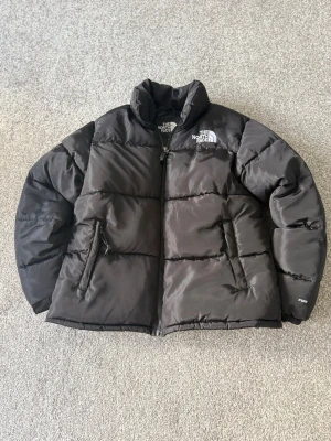Svart dunjacka från The North Face - Säljer en svart dunjacka från The North Face, modell 700. Jackan har hög krage, två dragkedjeförsedda fickor och klassisk logga på bröstet. Perfekt för kalla vinterdagar och riktigt skön att bära. Stängs med dragkedja framtill.