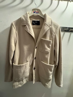 Beige fleece cardigan med fickor - Stilren beige cardiganjacka från antioch i mjuk fleece. Jackan har tre framfickor, knäppning med tre knappar och klassisk krage. Perfekt för lager på lager och en avslappnad look.