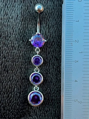 NY oanvänd Navelpiercing med hänge | Kirurgiskt stål | Lila stenar  - 💕30% Bundle-rabatt vid köp av minst 2 artiklar. ⭐️NY oanvänd piercing i kirurgiskt stål; rostfritt och säkert för läkta piercingar.                               📏MÅTT ⭕️Stavens längd: 10mm ⭕️Stavens tjocklek: 1,6mm ⭕️Smyckets totala längd: 50mm                                                                         🤍Färger: Silver och lila                                                          💌Skickas spårbart via Plick SafePay.