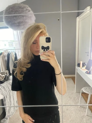 Svart stickad polotröja kort ärm - Säljer en svart stickad polotröja med korta ärmar. Tröjan har en hög krage och är gjord i ett mjukt, fluffigt material som känns riktigt cozy. Perfekt till jeans eller kjol för en clean look.