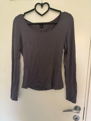 Mörkgrå långärmad topp - En enkel och stilren mörkgrå långärmad topp med rundad urringning. Tillverkad i mjukt och stretchigt material som sitter skönt mot kroppen. Perfekt att matcha med både jeans och kjol för en clean look. Finns en likdan fast blå i min profil