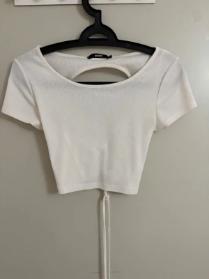 Vit ribbad croppad topp  - Trendig vit ribbad croppad topp från bikbok med korta ärmar och snygg snörning i ryggen. Toppen har en öppen ryggdetalj och är tillverkad i ett stretchigt material som sitter snyggt på kroppen. 