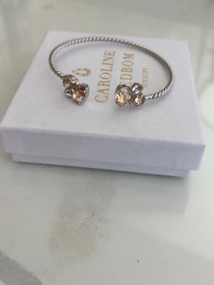 Caroline Svedbom armband med kristaller - Snyggt armband från Caroline Svedbom i silverfärgad metall med tvinnad design. Armbandet har stora, ljusgula kristaller och mindre klara stenar i varje ände som ger en lyxig känsla. Perfekt accessoar för att lyfta din outfit.