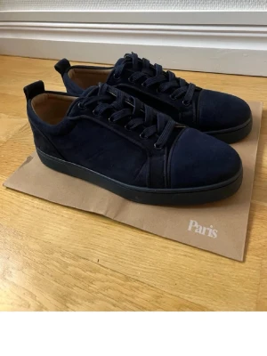 Mörkblå sneakers från Christian Louboutin - Snygga mörkblå sneakers i mocka från Christian Louboutin. Klassisk låg modell med rund tå, matchande mörkblå snörning och diskret logga på insidan. Yttersulan är svart och insidan är ljusbeige läder för extra komfort.