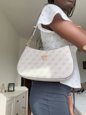 Väska från GUESS - Säljer denna supersnygga väska från GUESS.  Väskan är i mycket fint skick, nästintill som ny, och har använts sparsamt. Köpt på Zalando för cirka 1 700 kr förra året, därav priset. Perfekt storlek för det viktigaste och ger en trendig touch till vilken outfit som helst. Säljs då den inte kommer till användning.