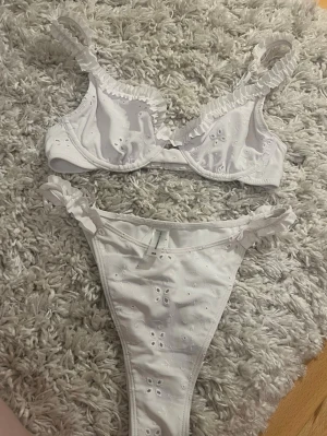 BikBok Vit bikini med volang och broderi - Söt vit bikini med volangdetaljer på axelbanden och broderade blommor. Överdelen har bygel och underdelen har knyt i sidorna. Perfekt för sommarens stranddagar!