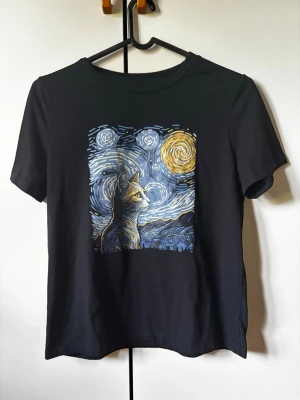 Svart t-shirt med kattmotiv - Svart t-shirt med coolt tryck av en katt i Van Gogh-inspirerad stil. Motivet har blå, gula och vita toner och ger en konstnärlig vibe. I använt fint skick.