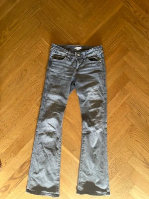Grå bootcut jeans från Gina Tricot - Säljer ett par grå bootcut jeans från Gina Tricot. Jeansen har klassisk femficksmodell, knappgylf och är tillverkade i mjukt denimtyg. Snygg tvättad look med utsvängning nedtill. Perfekta för en trendig och avslappnad stil. Fickorna där bak funkar inte och har inga knappar