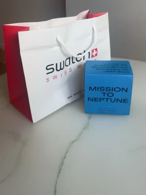 Swatch x Omega Mission to Neptune - Säljer en Swatch x Omega Mission to Neptune från Bioceramic MoonSwatch-kollektionen. Klockan har blå boett och svart urtavla med vita detaljer. Kommer i originalförpackning med tillbehör. Perfekt för dig som gillar unik design och coola färger.