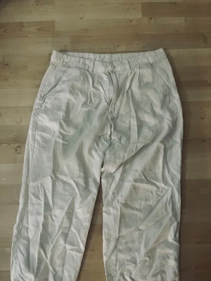 Beiga linnebyxor med raka ben - Snygga beiga linnebyxor med avslappnad passform och raka ben. Byxorna har sidfickor och stängs med knapp och dragkedja. Perfekta för en chill och stilren look. Materialet är luftigt linne som passar bra till varmare dagar.