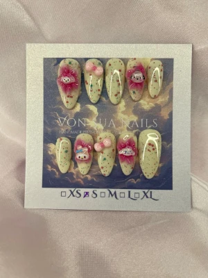 Melody (S);Medium Almond - Supergulliga handgjorda press-on naglar i pastellgul med färgglada prickar och 3D dekorationer som rosa rosetter, blommor och söta figurer. Medium långa almond naglar i S: 15 mm, 11,5 mm, 12 mm, 11 mm, 9 mm ,som verkligen sticker ut och ger en unik look.