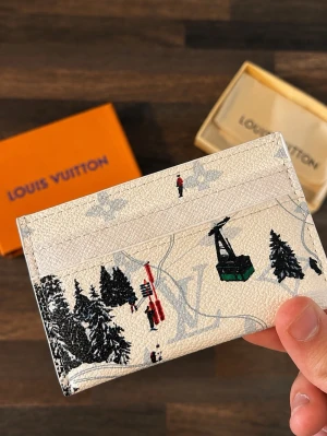 Louis Vuitton kortfodral vit - Säljer ett exklusivt kortfodral från Louis Vuitton i beige canvas med vinterinspirerat tryck av granar, skidåkare och lift. Klassisk LV-monogram syns i bakgrunden. Perfekt för kort och ID, smidig att ha i fickan. Lyxig och unik accessoar för dig som gillar designer.