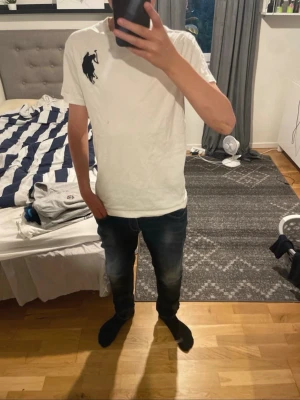 Vit t-shirt från us polo - Snygg vit t-shirt från us polo med den klassiska stora svarta polospelaren broderad på bröstet. T-shirten har rund hals och korta ärmar, perfekt till jeans eller shorts. Enkel och stilren design som funkar till det mesta. Har ett lite hål som syns på bilden, men syns knappsat på. Storlek S