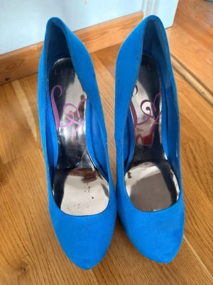 Blåa pumps med metallklack - Snygga blåa pumps från Lypsy london med spetsig tå och hög metallklack. Skorna har en slät ovandel i mockaimitation och en platåsula framtill för extra höjd. Insidan har ett coolt tryck med hjärtdetalj. Perfekta för dig som vill sticka ut.