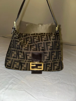 Fendi Mama Baguette handväska - äkta vintage fendi mama baguette handväska i brunt tyg med klassiskt FF-monogram. perfekt storlek för en handväska. köpt på retro tale för 11 000kr och har ett äkthetsbevis. väskan är i perfekt skick, förutom några ”skrapor” eller märken på själva magneten så är tyget felfri, inga rivmärken eller så. kan skicka bättre bilder/videos vid intresse. har använt väskan mindre än 5 gånger 