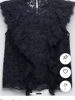 Mörkblå spetsblus med volang - Supersnygg mörkblå blus i spets med volangdetaljer framtill och vid ärmslut. Blusen är ärmlös och har en hög halsringning. Perfekt att styla med jeans eller kjol för en trendig look.