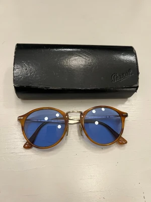 Persol Calligrapher Edition PO 3166S 960/56 - Det traditionella märket, Persol, har stått för utmärkt italiensk hantverkskonst i över 90 år. Än idag ligger fokus på högsta kvalitet, briljans och teknisk innovation. Alla glasögonmodeller är handgjorda i den historiska fabriken i Lauriano, vilket gör dem både legendariska och unika. Glasögonmodellerna går enkelt att känna igen tack vare den omisskännliga Supreme-pilen och den underliggande retro-charmen som påminner om svunna tider. ***Jättefint kondition ingen skador eller repor.