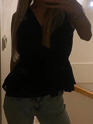 Svart v-ringad topp med volang - Snygg svart fest topp med v-ringning och volang nedtill. Jätte najs och perfekt för alla möjliga saker. 