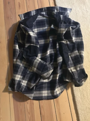 Blåvit rutig skjorta i bomull - Säljer en blå och vit rutig skjorta med klassisk krage och långa ärmar. Skjortan har en bröstficka och knappar framtill. Perfekt för dig som gillar en avslappnad men ändå stilren look.