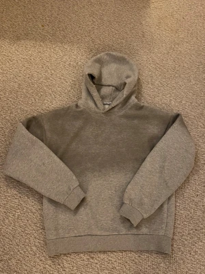 Grå hoodie från Acne Studios - Snygg grå hoodie från Acne Studios i mjuk bomullsblandning. Klassisk modell med huva och ribbade muddar vid ärmar och nederkant. Perfekt för en avslappnad och stilren look. Diskret logga i nacken och neutral färg som passar till allt.