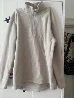 Ljusgrå fleece-tröja med halv dragkedja - Mysig ljusgrå fleece-tröja med hög krage och halv dragkedja framtill. Tröjan har lång ärm och är tillverkad i mjukt fleecematerial som håller dig varm. Perfekt för lager-på-lager och chill dagar.