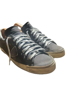 Blå sneakers från Philippe Model - Snygga blå sneakers från Philippe Model med vita detaljer och vita skosnören. Skorna har en låg silhuett och en beige, något sliten sula. Ovandelen är i mocka och läder, och hälen har en vit kontrast. Perfekta för en avslappnad streetstyle.